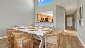 A dining area with a white table, six wicker chairs, and a kitchen visible through an open door. - Fairway View Escape in Palm Desert (Palm Desert)