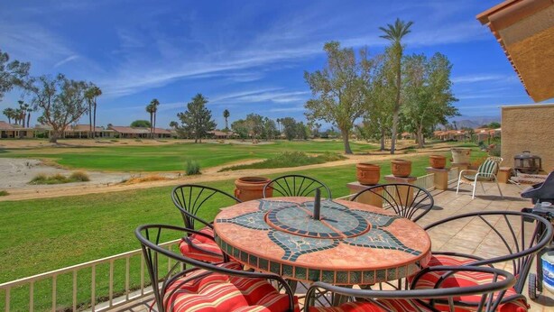 Une terrasse extérieure avec une table ronde et des chaises, une vue sur un terrain de golf et un ciel bleu dégagé.