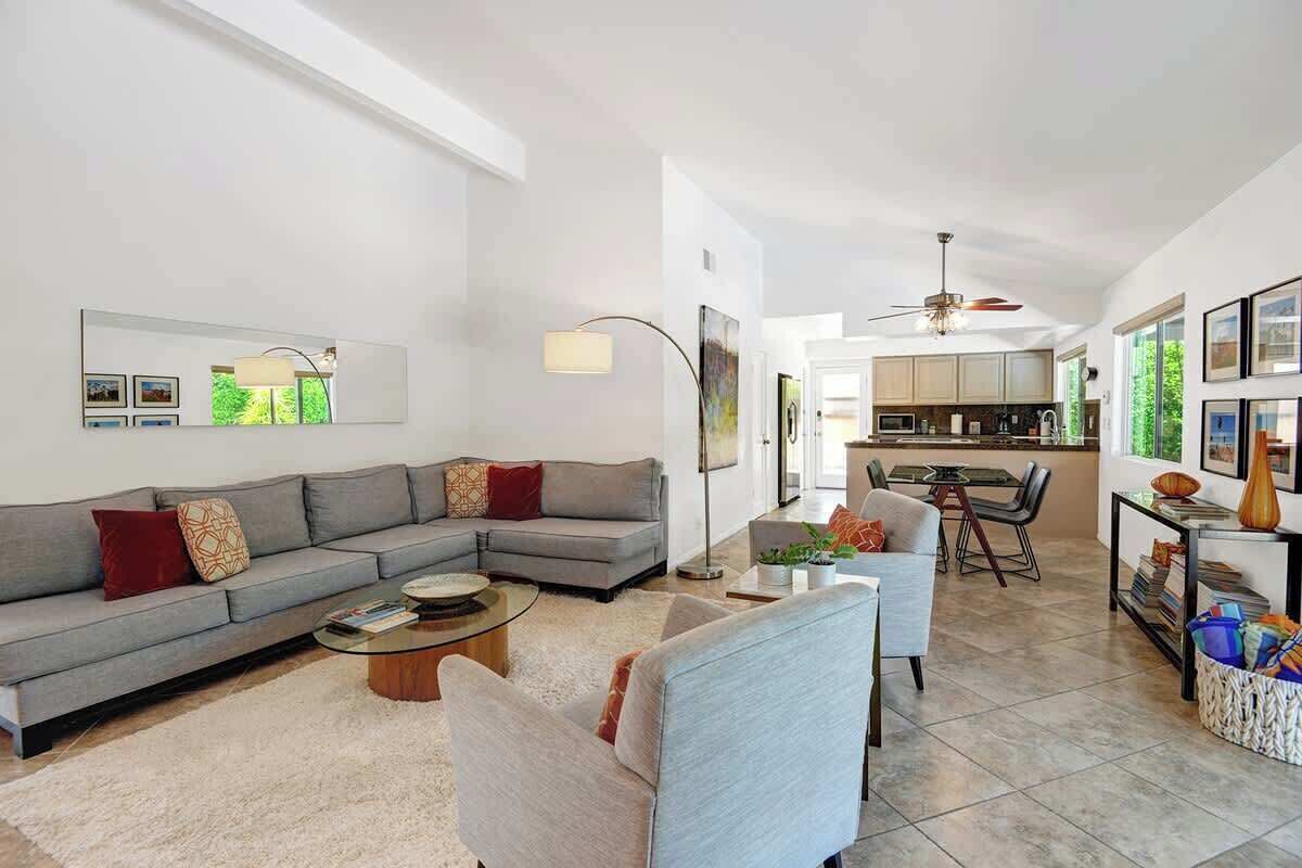A modern living room with a grey sectional sofa, a coffee table, and a dining area with a kitchen in the background.