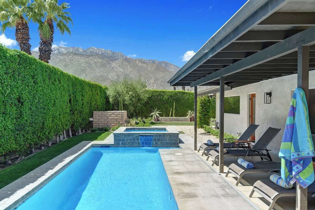 A swimming pool with a mountain backdrop, lounge chairs, and a pergola.