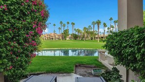 A view of a golf course with a pond, palm trees, and a building in the background. - Beautiful Views-Resort Living (Palm Desert)