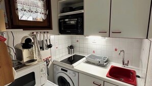 Ett kompakt kök med tvättmaskin, mikrovågsugn, diskho och spis.