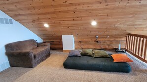 Un dormitorio tipo loft acogedor con techo de madera, un sofá marrón, un sofá verde con cojines y un radiador blanco.