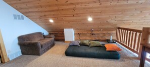 A cozy loft bedroom with a wooden ceiling, a brown sofa, a green sofa with cushions, and a white radiator.