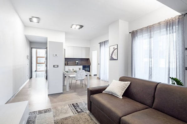 Ein modernes Wohnzimmer mit einer Couch, einem Essbereich und einer Küche im Hintergrund.