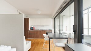 A modern kitchen with white cabinets, a dining area with a table and chairs, and a large window providing natural light. - GuestHost - Cozy Studio in Portello District (Milano)