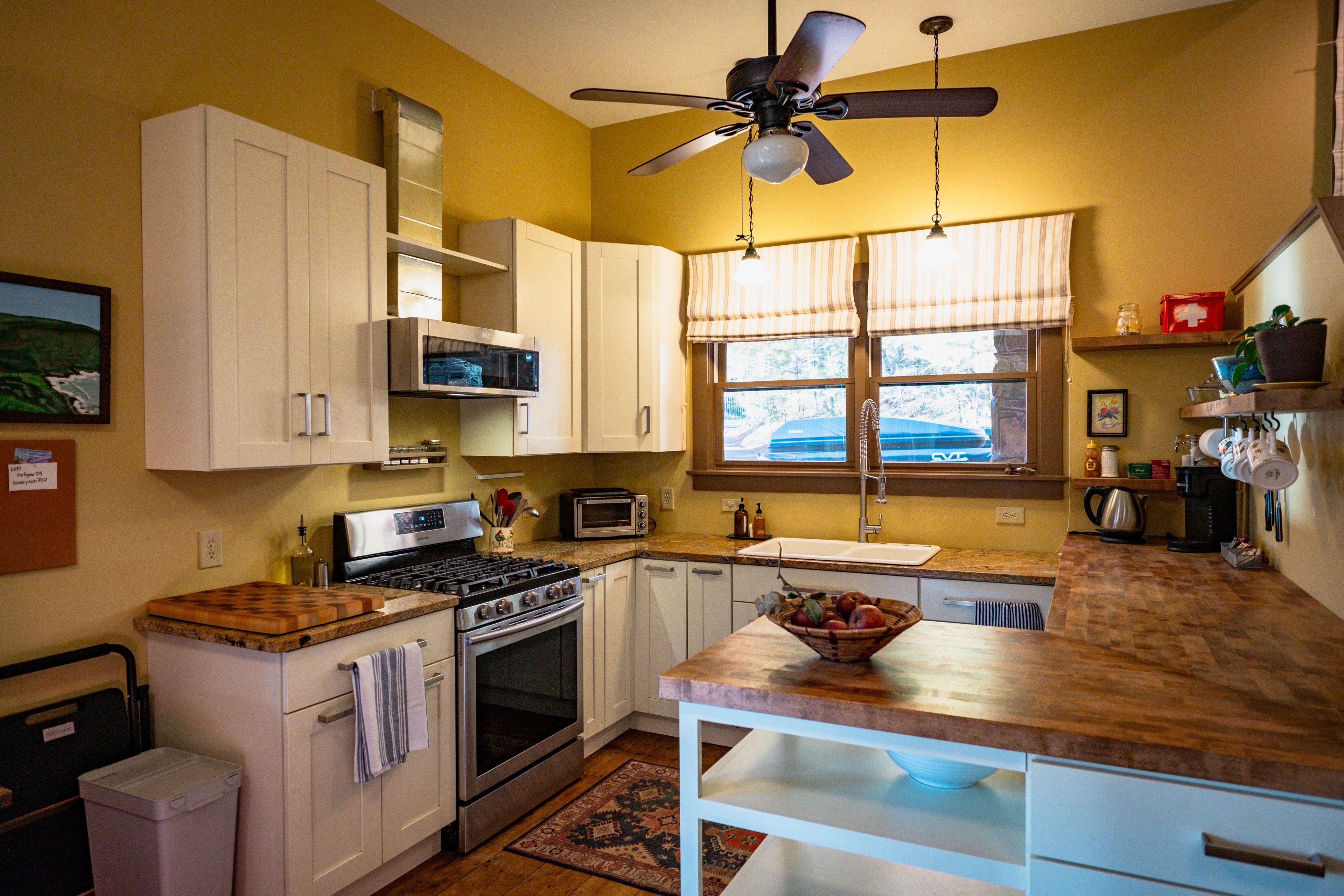 A kitchen with white cabinets, a microwave, a stove, and a ceiling fan.