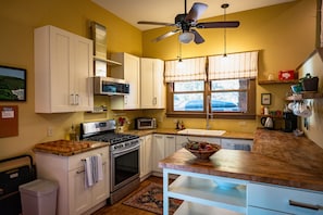 A kitchen with white cabinets, a microwave, a stove, and a ceiling fan.