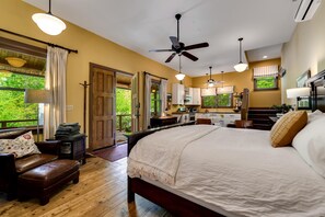 A bedroom with a large bed, a sitting area with a bench, and a view of the outdoors through a door. - Hazel Studio - King Bed Studio with Twin Bunkbeds in side room. Full kitchen, bathroom and covered front porch. (Franklin)