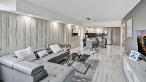 A modern living room with a grey sofa, a coffee table, and a kitchen in the background. - Sunny Isles Resort by the beach w/ Pool, Games & Gym (Sunny Isles Beach)