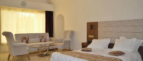 Una habitación de hotel con cama, sofá, dos sillones, una mesa de centro y alfombra.