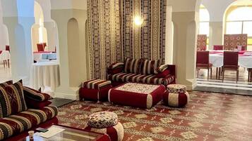 Un'elegante area relax con tappeti decorati, divani rossi e un soffitto alto con drappeggi.