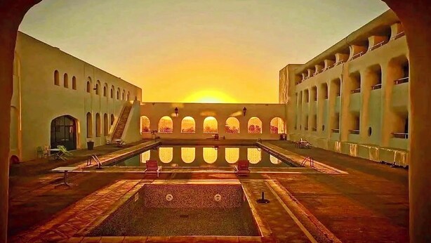 A courtyard with a central pool, surrounded by buildings with arched windows and a staircase leading to an upper level. - Mzab Hotel (Ghardaïa)