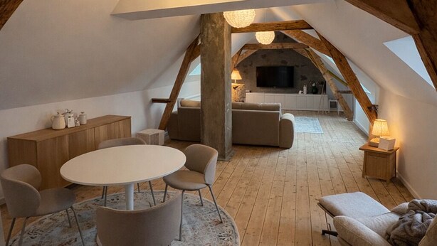 Een gezellige zolderkamer met een houten plafond, een ronde eettafel en een bank.