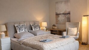 Een slaapkamer met een groot bed, nachtkastjes, een hanglamp, een stoel en een vloerkleed.