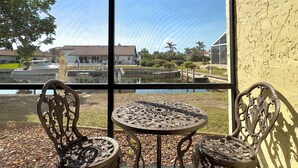 A balcony with a table and two chairs, overlooking a residential area with houses and a body of water. - A  Punta Gorda 1 Bed Waterfront 1st-Floor Condo -Walk to Fishermen’s Village (Punta Gorda)