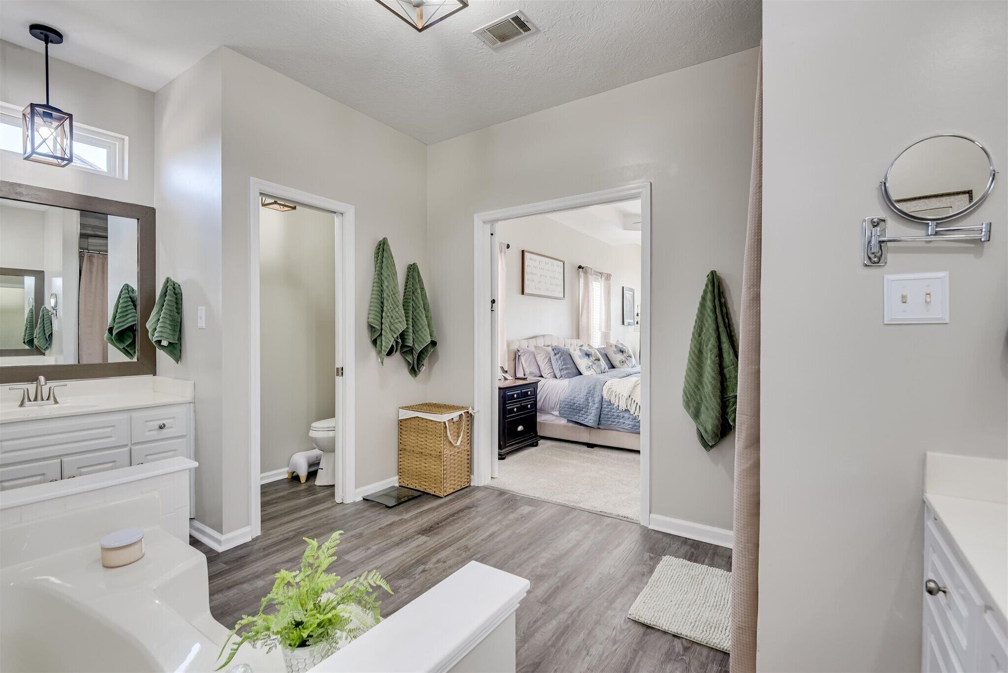 A modern bathroom with a white vanity, a large mirror, and a green plant.