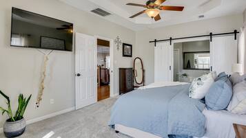 A bedroom with a bed, a ceiling fan, a TV, and a door leading to another room.