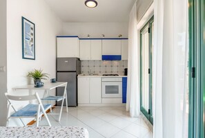 A compact kitchen with white cabinets, a refrigerator, an oven, and a dining area with a table and chairs. - GuestHost - Romantic Retreat in Taormina (Taormina)