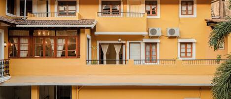 A two-story building with a yellow facade, multiple windows with curtains, and balconies.