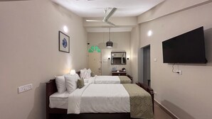 A hotel room with two beds, a ceiling fan, a flat-screen TV, a framed picture, and a mirror. - Pousada St. Ines Boutique Stays (Panaji)