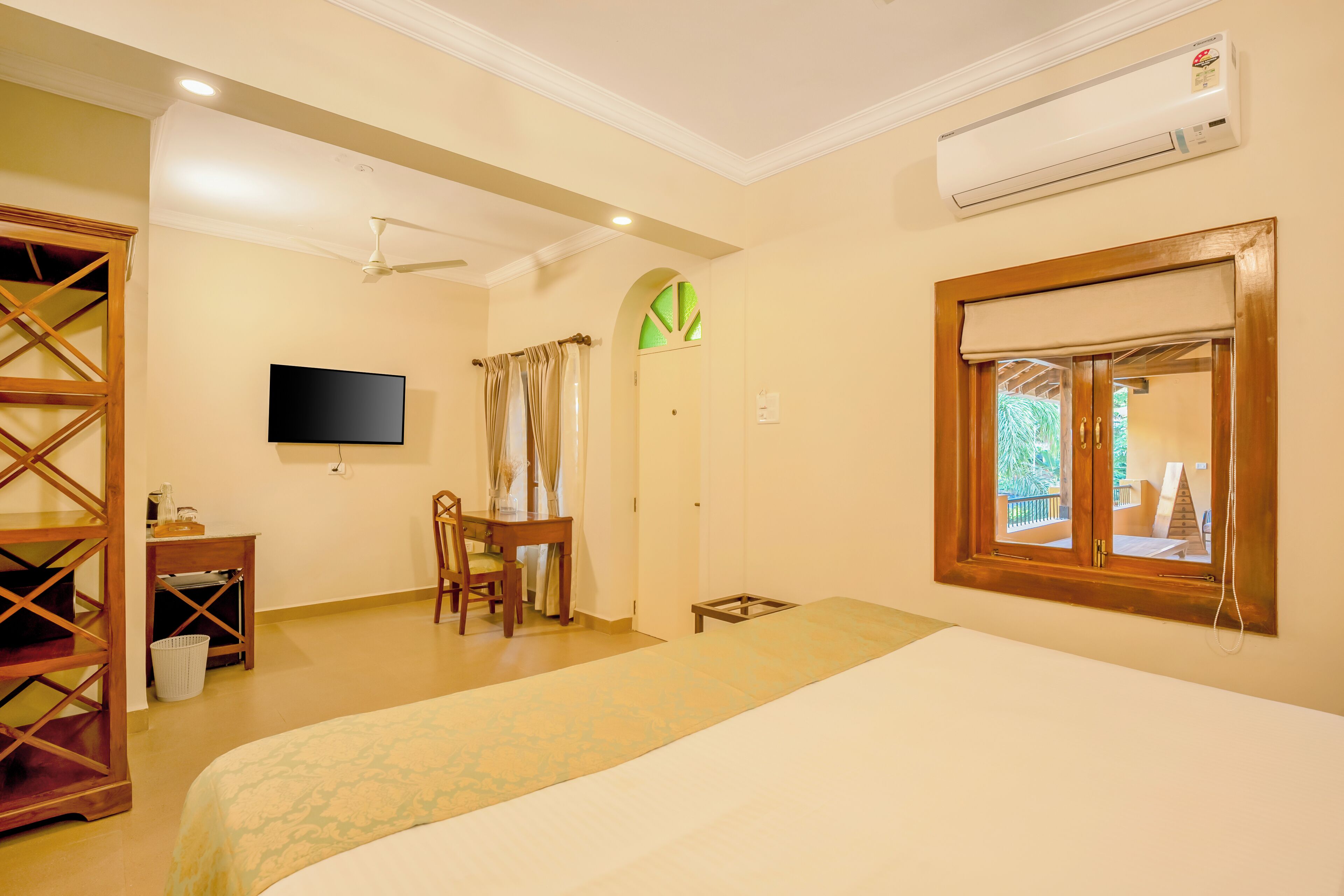 A hotel room with a bed, a desk, a chair, a television, an air conditioner, and a window with a view of the outside.
