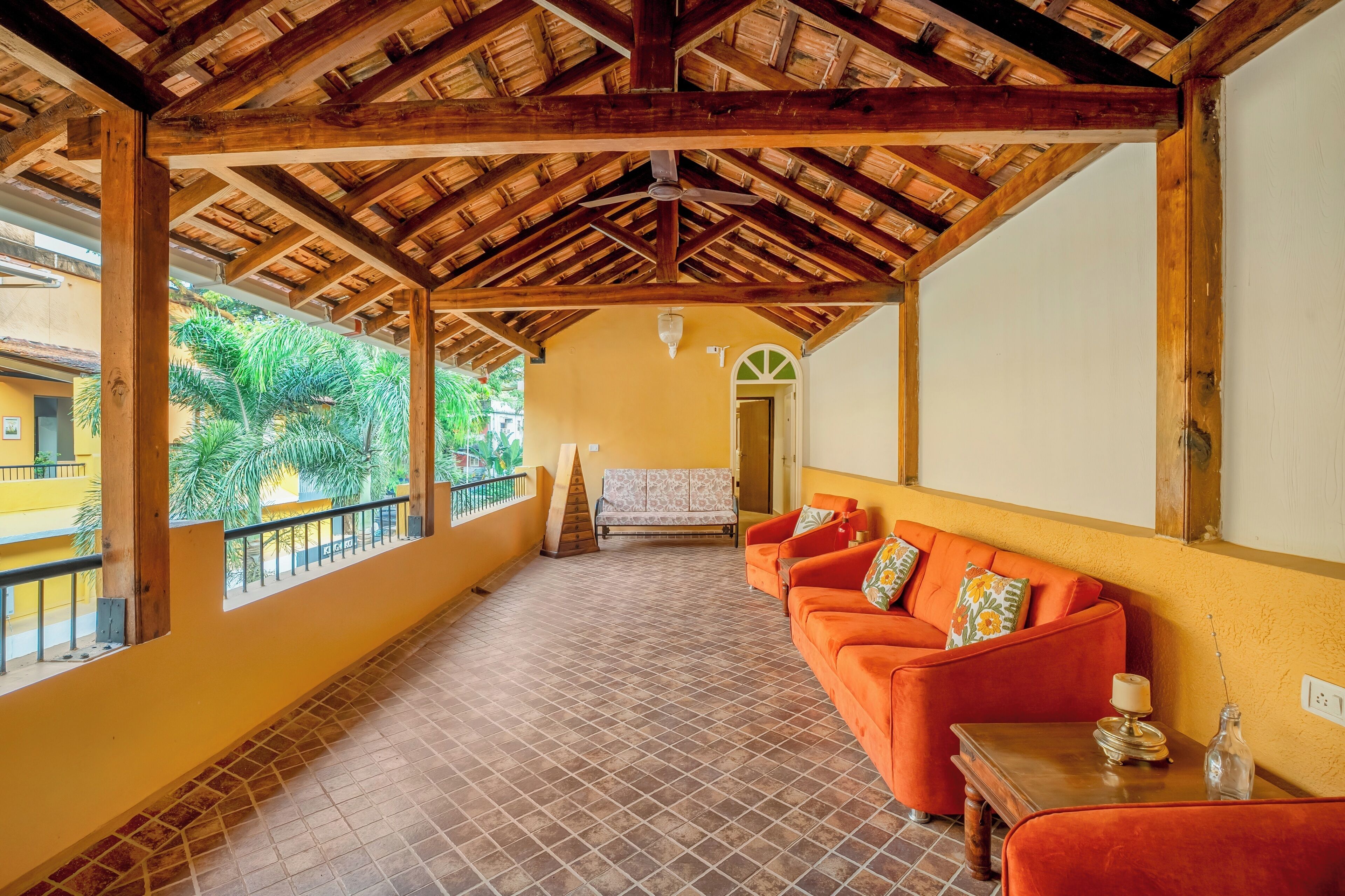 A covered outdoor area with a wooden ceiling, a tiled floor, and a seating area with orange sofas and a bench.