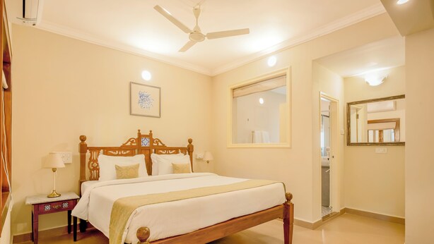 A hotel room with a wooden bed, bedside tables, a ceiling fan, and a large mirror. - Pousada St. Ines Boutique Stays (Panaji)