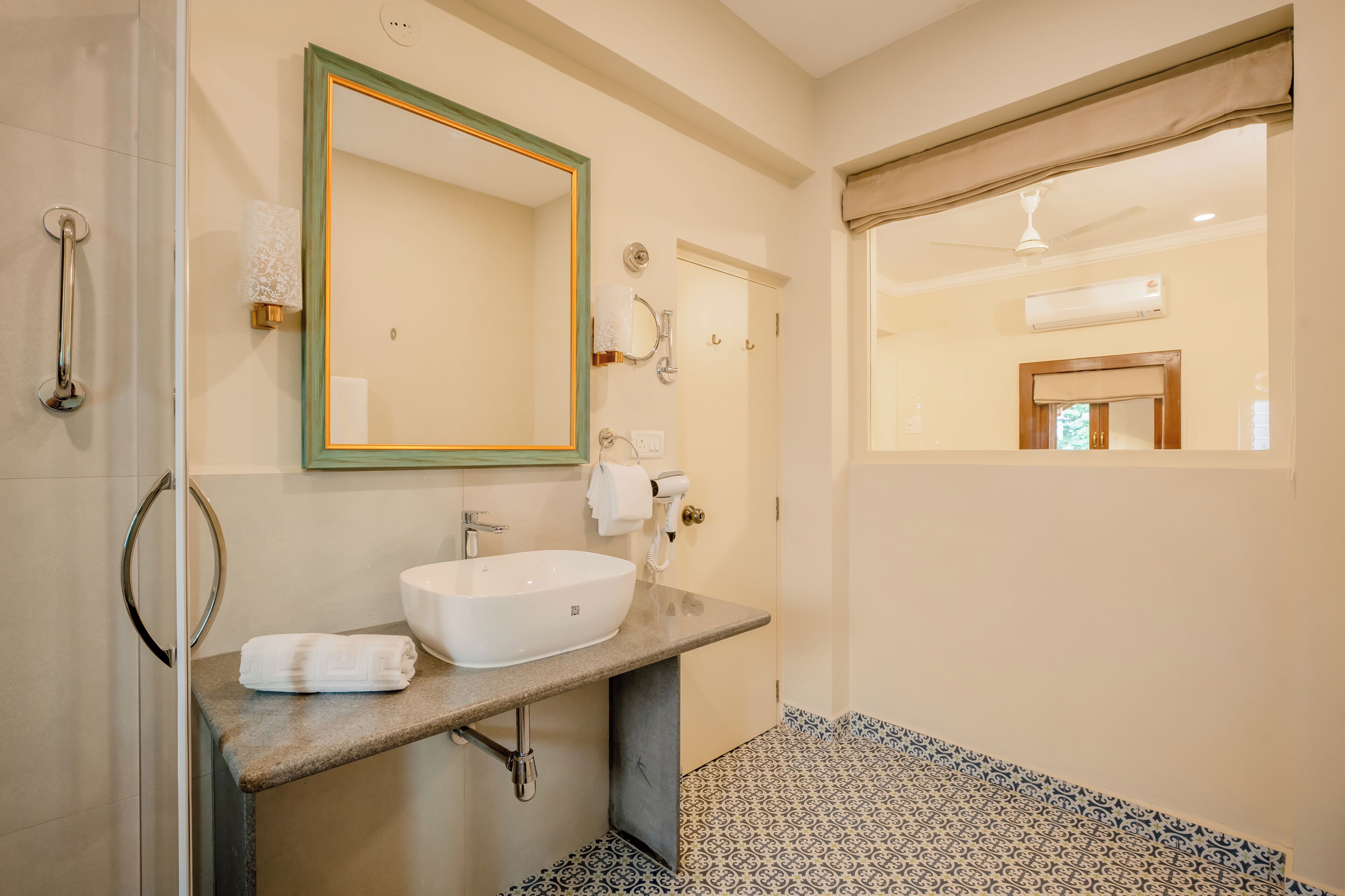 Un baño con un espejo grande, lavamanos, toalla, ducha y ventana.