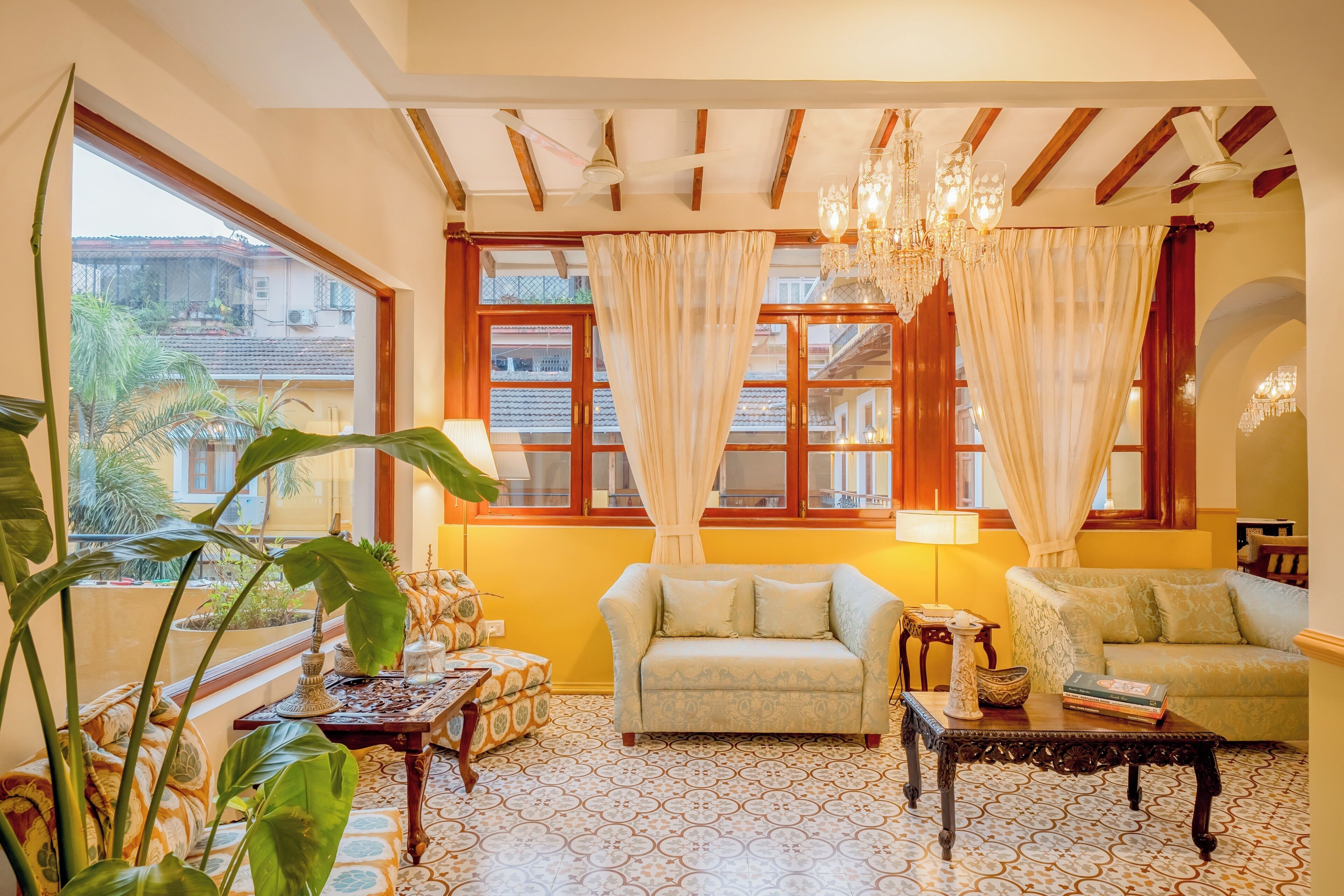 Un salón acogedor con dos sofás, una mesa de centro y una araña. Se ven grandes ventanales con cortinas y vistas a edificios.