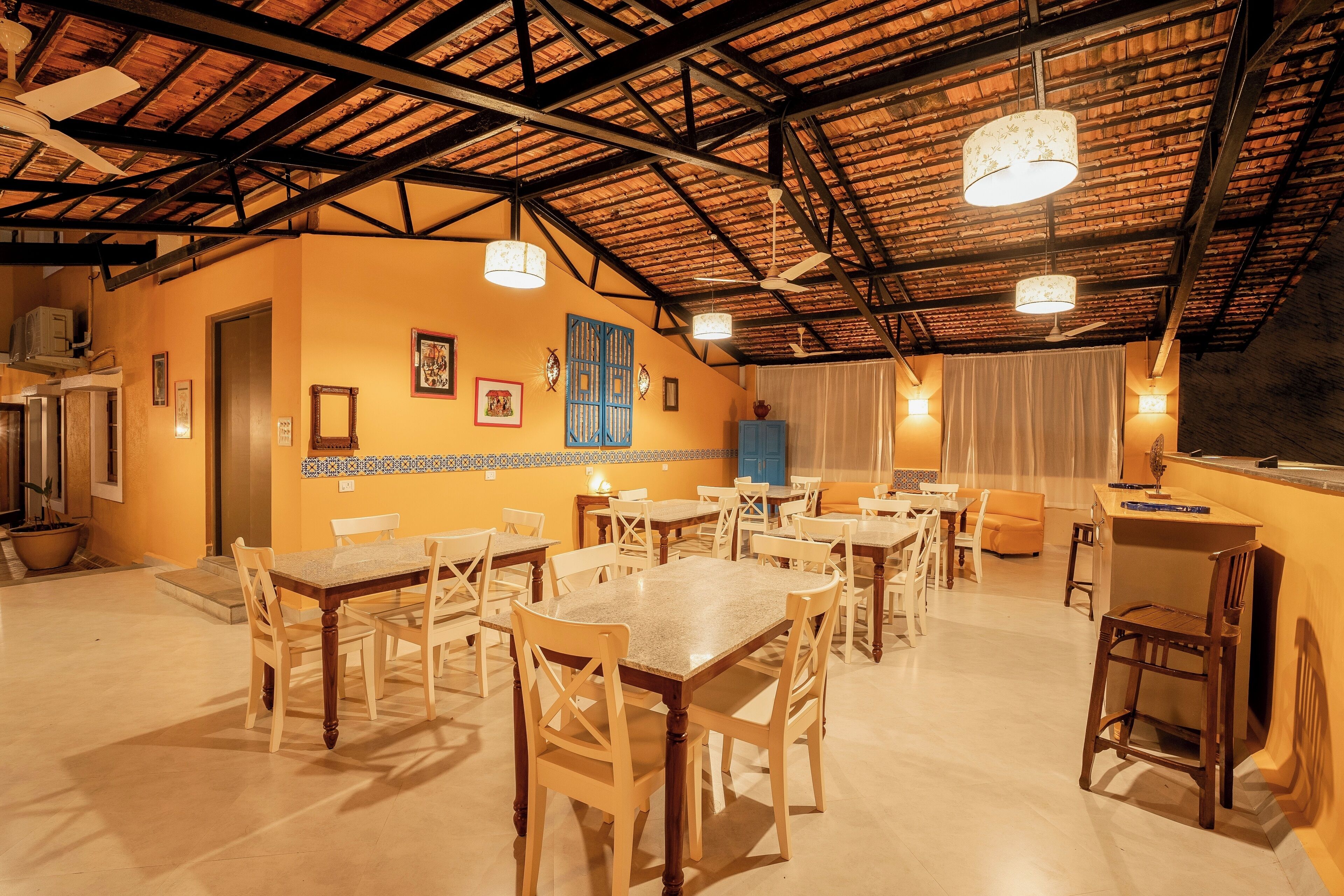 A dining area with multiple tables and chairs, a ceiling with exposed beams, and a kitchen area with a counter and sink.