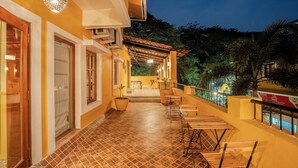 A covered outdoor area with tiled flooring, wooden furniture, and a railing overlooking a garden. - Pousada St. Ines Boutique Stays (Panaji)