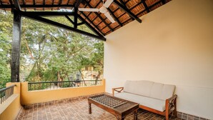 A balcony with a wooden table and sofa, a tiled floor, and a view of trees and buildings. - Pousada St. Ines Boutique Stays (Panaji)