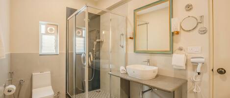 Un baño moderno con ducha de vidrio, un lavabo blanco y un espejo con marco dorado.