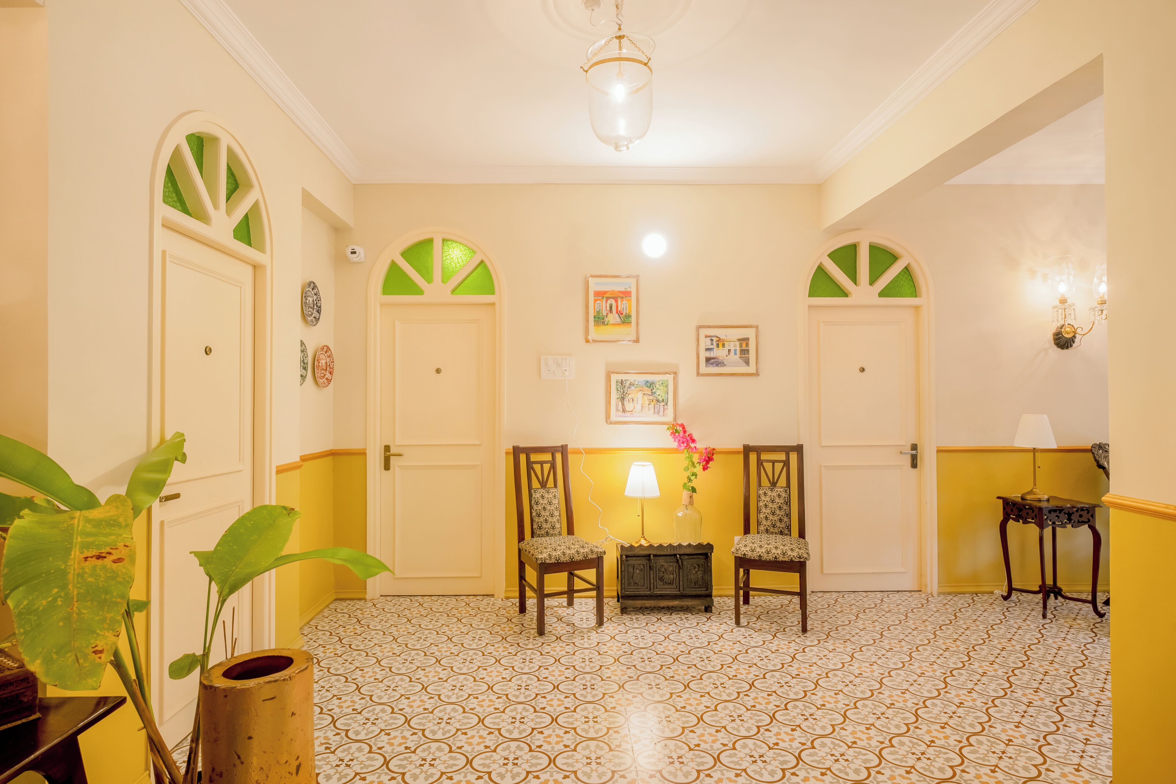 A room with a patterned floor, two chairs, a small table, and a wall-mounted lamp.