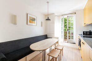A modern kitchen with a dining area, a bench, and a view through a glass door. - Elegant Two Bed Near Shoreditch (London)