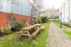 A paved pathway with picnic tables and a brick wall with a metal fence. - Elegant Two Bed Near Shoreditch (London)