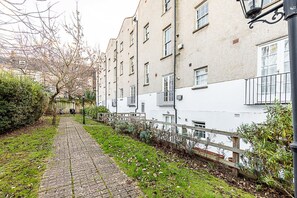 A narrow cobblestone pathway flanked by buildings with white and beige facades, a wooden fence, and a lamppost. - Elegant Two Bed Near Shoreditch (London)