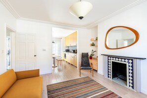 A modern living room with a sofa, a striped rug, a fireplace, and a kitchen in the background. - Elegant Two Bed Near Shoreditch (London)