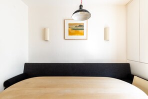 Ein Zimmer mit einem Holztisch, einer schwarzen gepolsterten Bank, einer Pendelleuchte und einem gerahmten Landschaftsbild an der Wand.