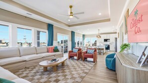 Uma sala de estar ampla, com um sofá, poltronas, uma mesa de centro e um tapete xadrez.