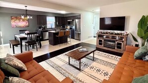 A modern living room with a sofa, coffee table, and TV. There is a kitchen area with cabinets and appliances. - Walk to Convention Centre, Restaurants, Falls! 3BR (Niagara Falls)