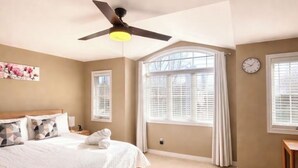 A bedroom with a bed, ceiling fan, large window with blinds, and a clock on the wall. - Walk to Convention Centre, Restaurants, Falls! 3BR (Niagara Falls)