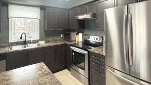 A modern kitchen with dark cabinets, stainless steel appliances, and a granite countertop. - Walk to Convention Centre, Restaurants, Falls! 3BR (Niagara Falls)