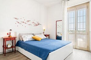 Ein Schlafzimmer mit einem Bett, einem Nachttisch, einer Lampe, einem Fenster mit Vorhängen und einer Wanddekoration.