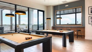Una mesa de billar con bolas, otra mesa y una zona de bar con taburetes.