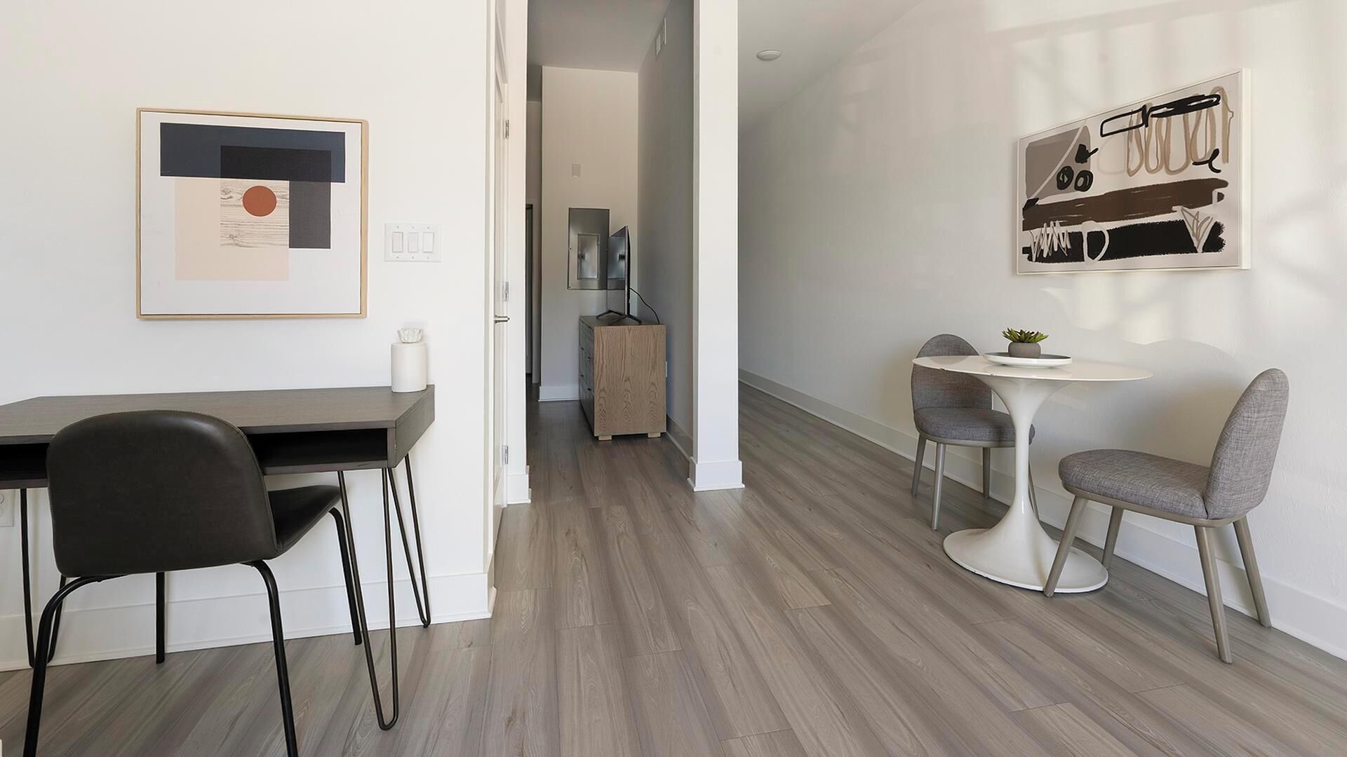 A modern, minimalistic room with a dining area, a small table with two chairs, and a kitchen visible in the background.