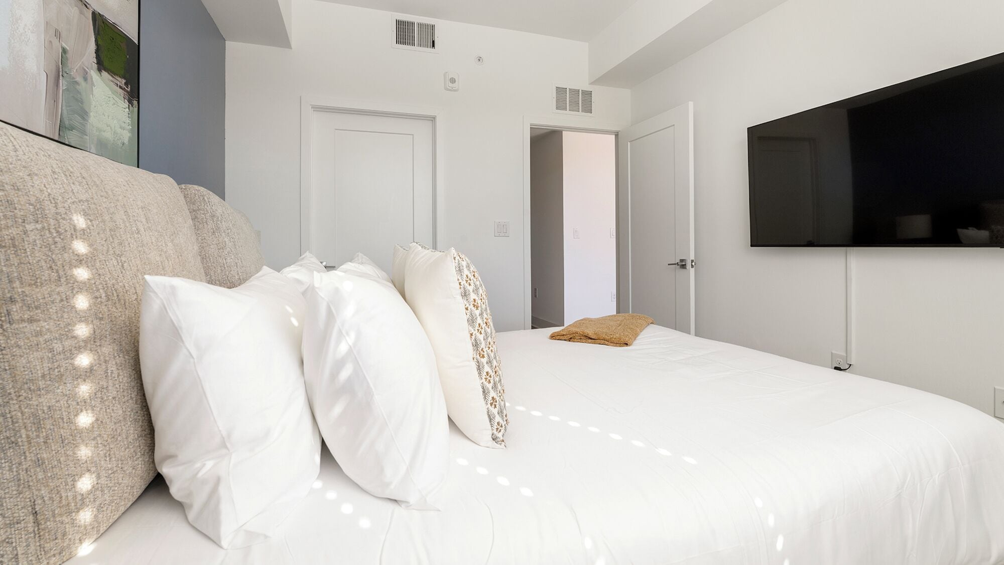A modern bedroom with a large bed, white bedding, and a mounted TV.