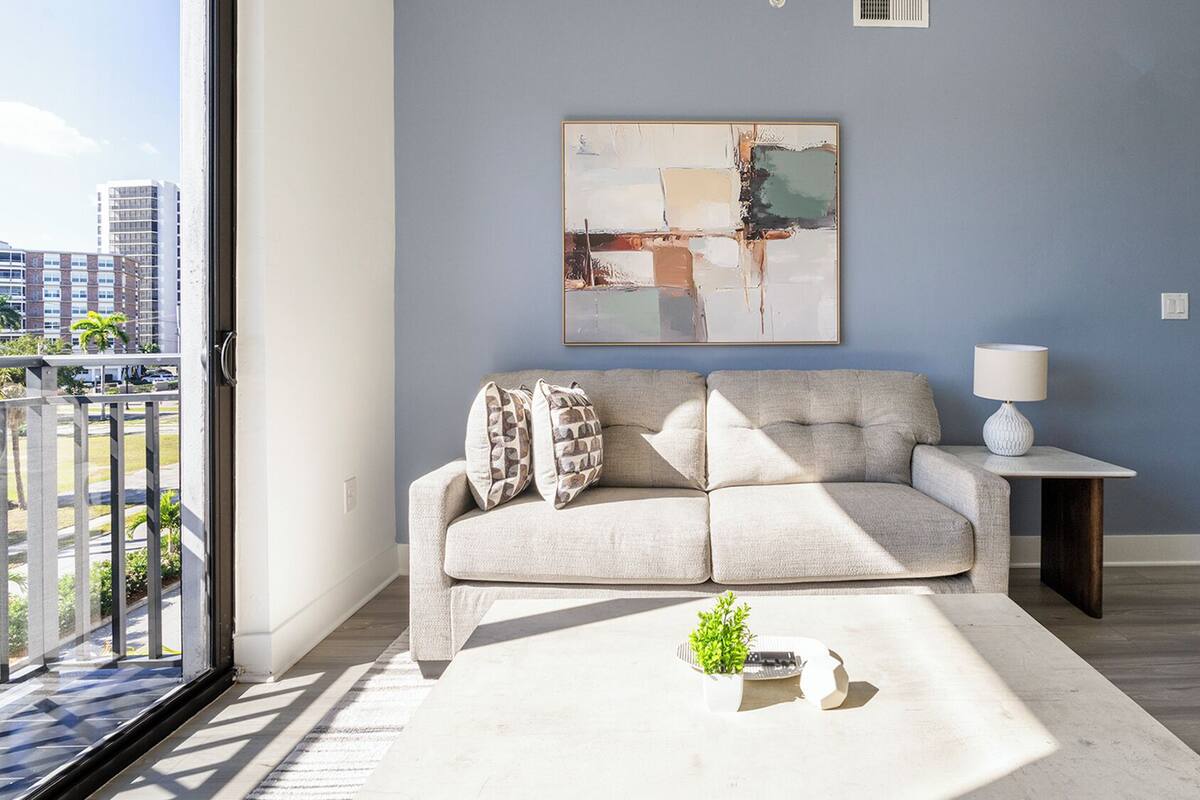 A modern living room with a grey sofa, a small table with a lamp, and a painting on the wall.
