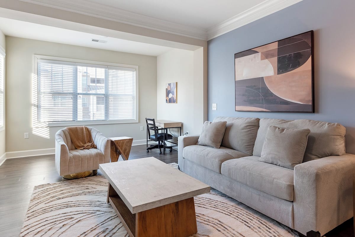 A modern living room with a sofa, armchair, coffee table, and a painting on the wall.